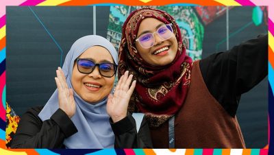 Two conference attendees wearing headscarfs smile and pose in front of a map display