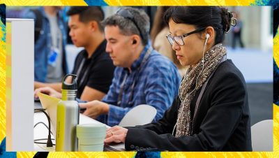 Several people seated at a table work on computers with maps and data visible on their screens in a conference setting
