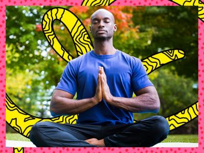 Person seated cross-legged outdoors in a park with hands in a prayer position practicing yoga