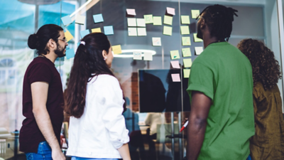 Four people looking at a glass office wall with sticky notes lined vertically