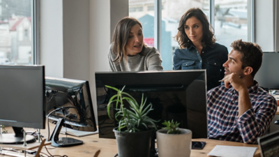 Three people surrounding a desktop computer talking about what is on the screen