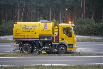 Gele vrachtwagen van Aannemersbedrijf Van Doorn op de weg met bomen op de achtergrond