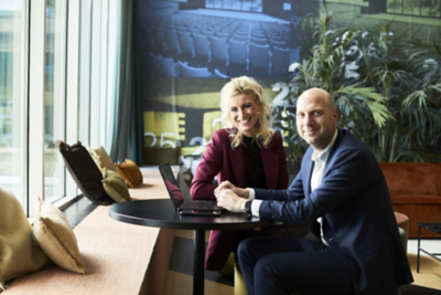 Esri Nederland collega’s werken samen rond een laptop aan een tafel in een moderne kantoorruimte met planten en een kaartvisualisatie op de achtergrond.