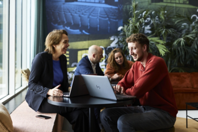 Esri Nederland collega’s werken samen rond een laptop aan een tafel in een moderne kantoorruimte met planten en een kaartvisualisatie op de achtergrond.