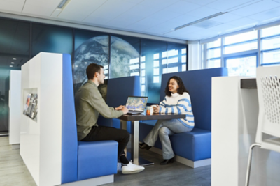 Twee personen zitten aan een tafel in een moderne kantoorruimte bij Esri Nederland, met een wereldkaartvisualisatie op de muur.