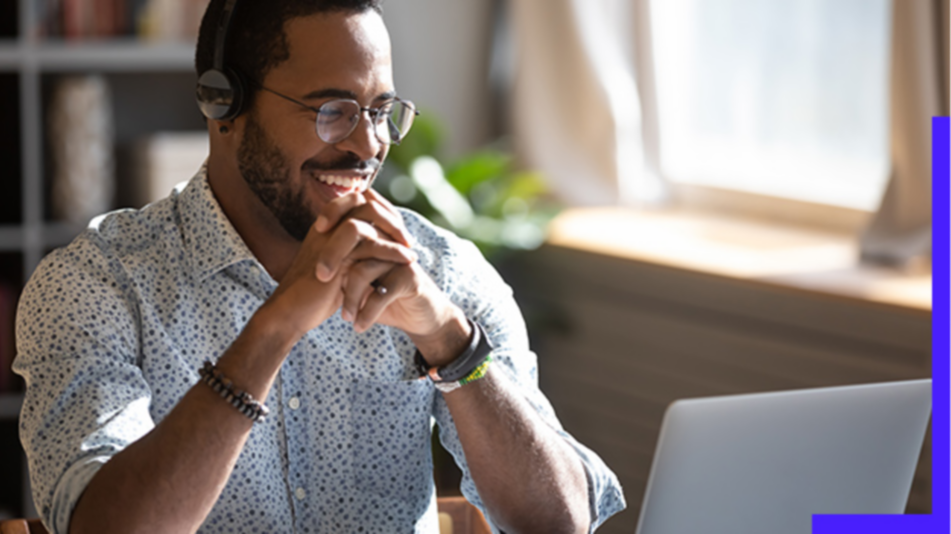 Person wearing glasses, seated at a desk, smiling and looking at a laptop screen