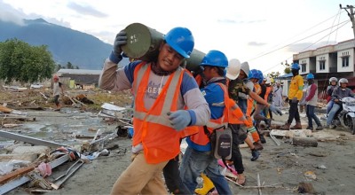 Men in orange vest and hard hats carrying a pole. 