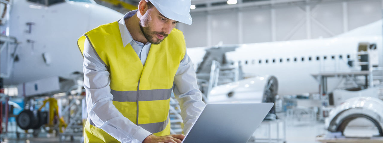 Un impiegato lato aria con casco e gilet alta visibilità che controlla le informazioni su un laptop