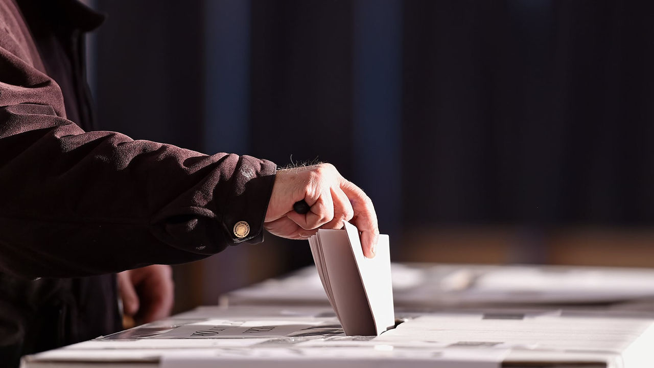 一位选民正在将纸质选票投入选票箱的投票口中。